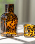 Amber glass carafe and drinking glass with black speckles on a light surface.