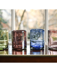 A set of four colored glass rocks glasses etched with stars, placed on a table with a window in the background.