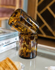 Tortoiseshell-patterned glass container on a surface with books and a decorative item in the background