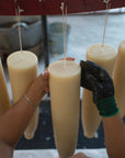Hands working with white candles hanging from a rack.