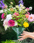 A colorful floral arrangement in a clear, fluted glass vase held by a person.