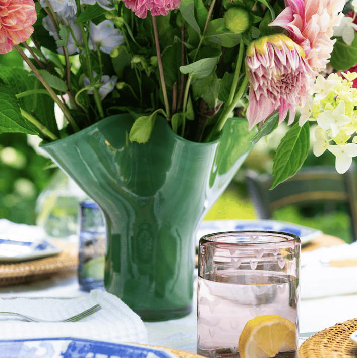 Green glass vase with flowers on a table with other glass wares