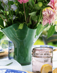 Green glass vase with flowers on a table with other glass wares