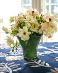 A petite green glass vase with flowers on a table