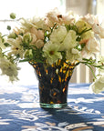 A petite lettuce leaf vase with a brown tortoise pattern containing flowers, placed on a table with a blue floral tablecloth.