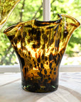 A handcrafted brown glass vase with a lettuce leaf design, sitting on a white surface with a blurred background.