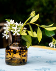 Small brown glass vase with white flowers and green leaves on a light blue tablecloth.