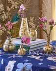 A selection of hand-blown glass vases with 14k gold leaf detailing, displayed on a table with floral patterns and containing floral arrangements.