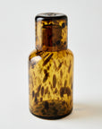 Brown glass bottle with a patterned cap on a white background