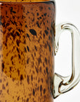 Speckled brown pitcher with a clear handle on a white background