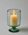 Green glass candle holder with a lit candle on a gray background