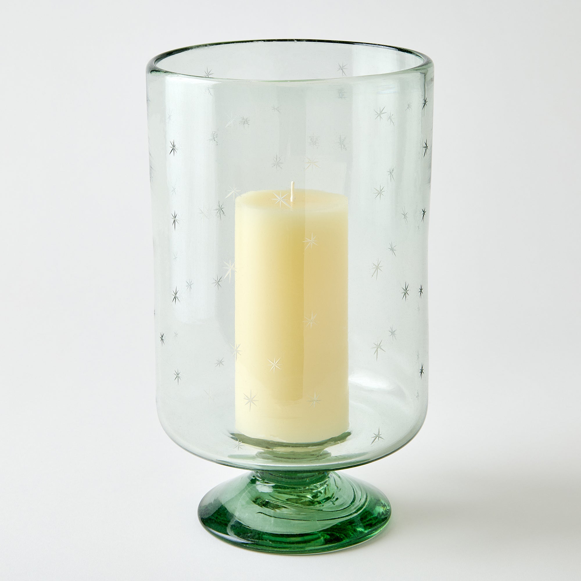 Clear glass candle holder with a clear base containing a white candle on a white background