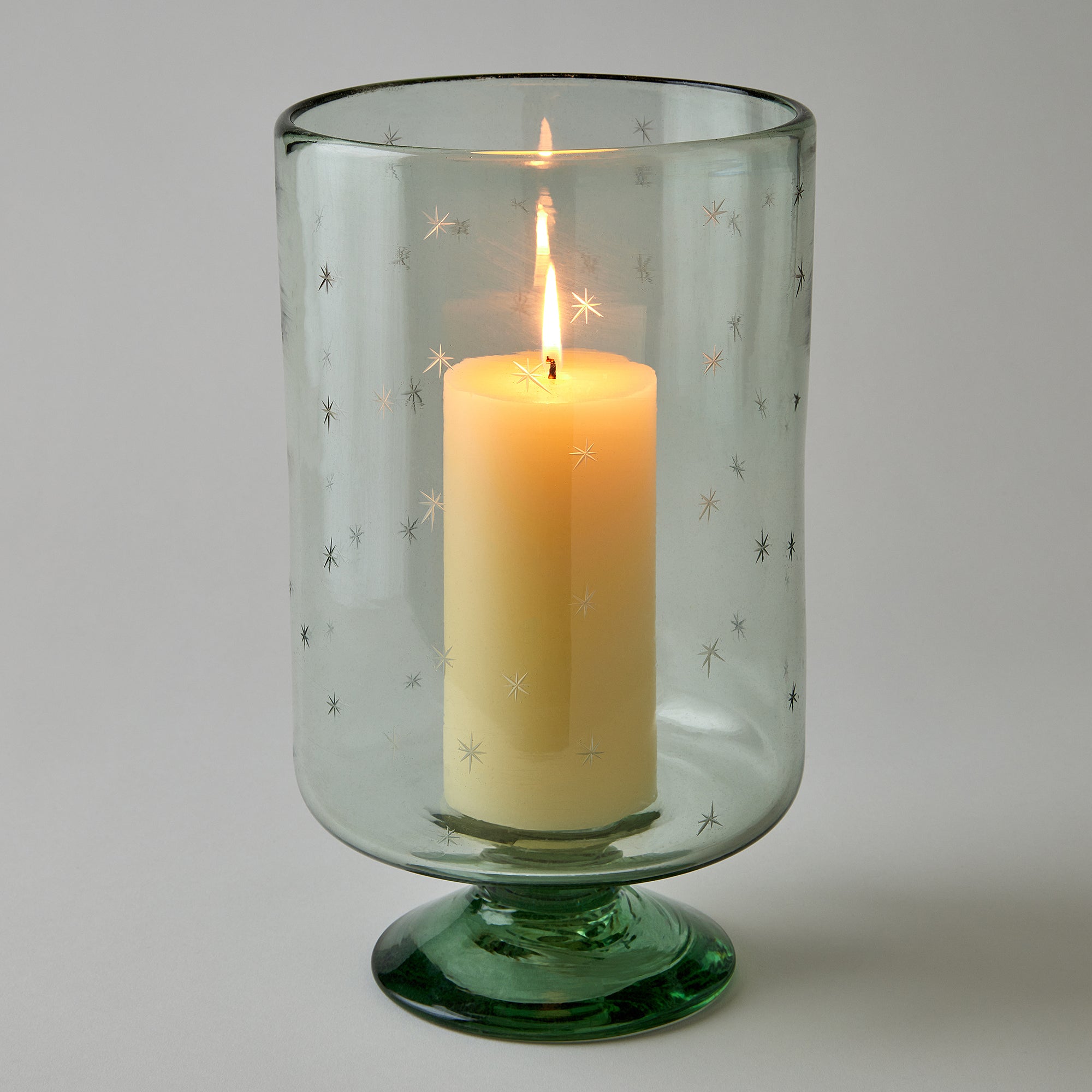 Candle in a green glass holder with star patterns on a gray background