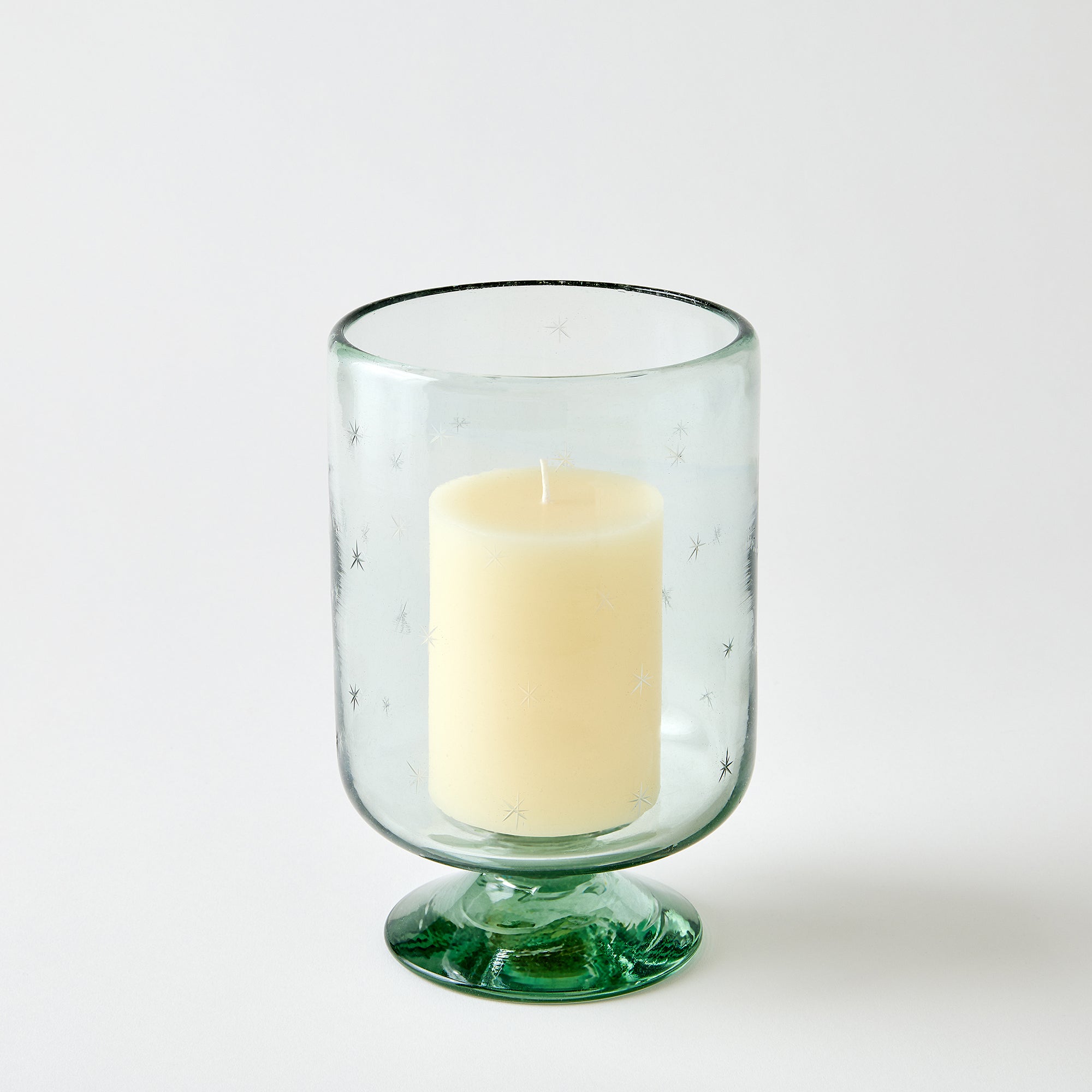 Clear glass candle holder with a white candle on a white background
