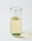 Clear glass filled with white sparkling wine on a light gray background