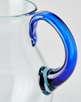 Clear glass pitcher with a blue handle on a light gray background