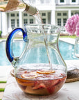 Glass pitcher with blue handle being filled outdoors by a poolside