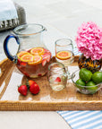 Tray with a pitcher of fruit-infused drink, glasses, vases, bowls, and fruits by a poolside.