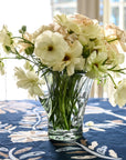 A clear glass vase with a starry base design, containing a bouquet of flowers, placed on a table with a blue floral tablecloth.