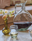 Glass decanter with red wine, glass of white wine, small vase with flowers, and bowl of snacks on a table.