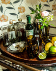Bar tray with bottles, glasses, and a floral arrangement against a patterned wall.