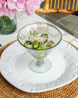 Dining table setting with pink flowers, glass dish, and cutlery on a white tablecloth.
