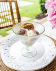 Ice cream dessert in a glass bowl on a white plate with pink flowers in the background
