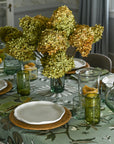 Dining table set with floral centerpiece, plates, and glasses in a room with curtains and a window.