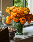 A clear glass vase with a fern motif, containing orange and yellow flowers, placed on a surface.