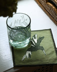 Clear glass with water on a green coaster with a deer design, placed on a white surface.