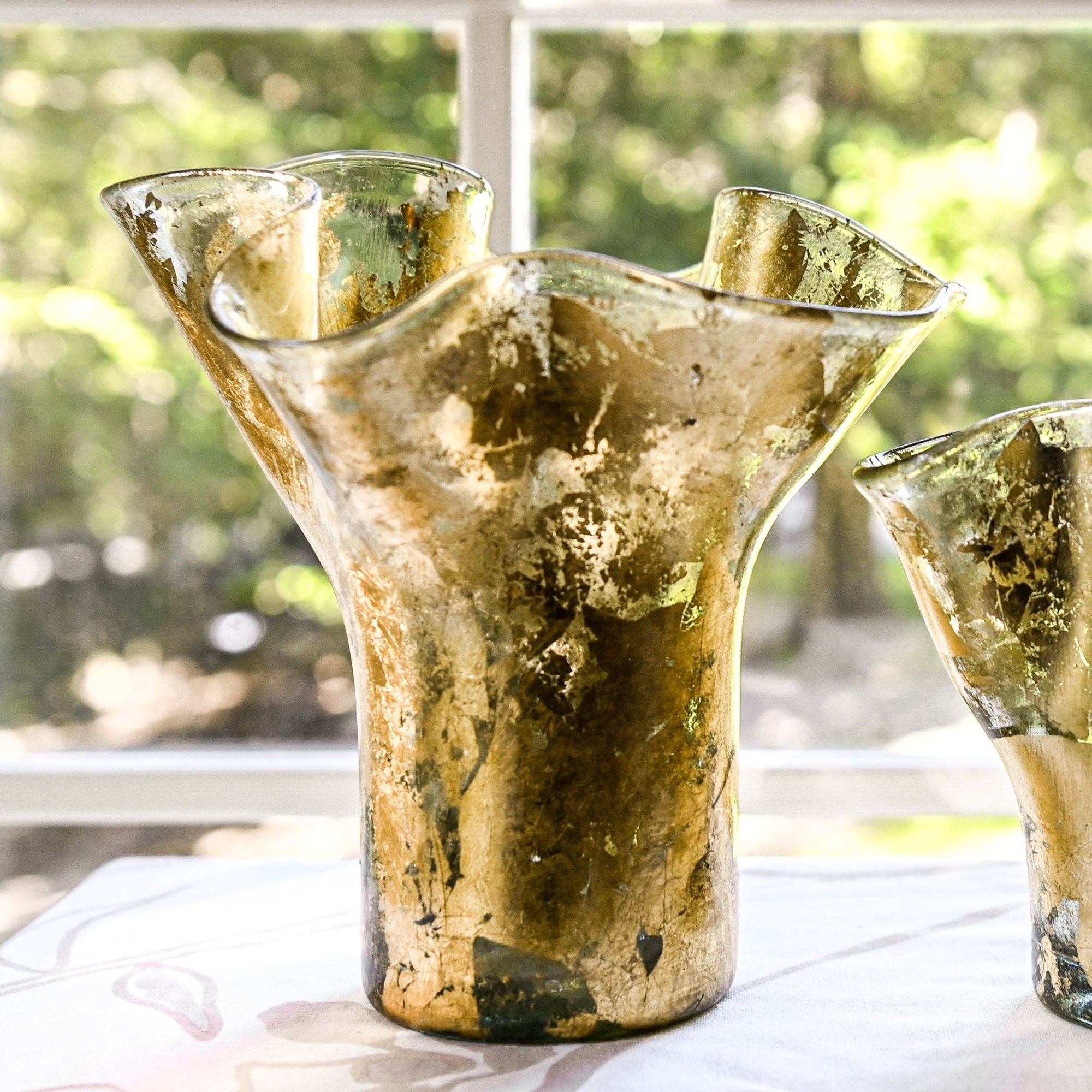 A gold leaf lettuce leaf vase with a unique shape, displayed indoors with natural light in the background.