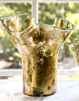 A gold leaf lettuce leaf vase with a unique shape, displayed indoors with natural light in the background.
