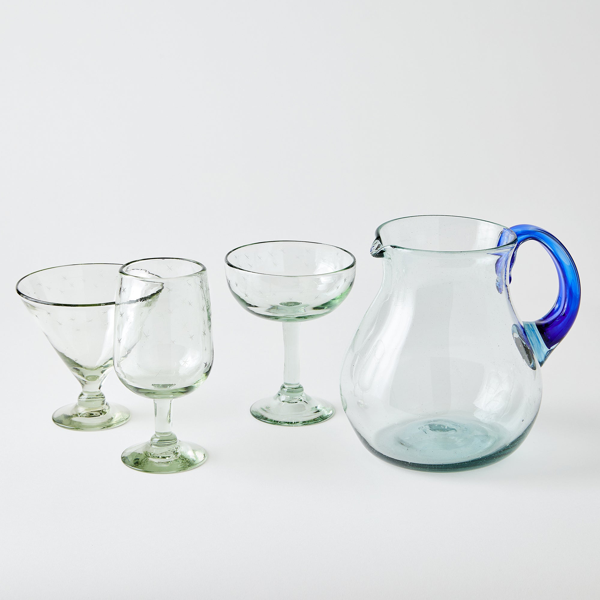 Set of clear glassware including a pitcher with a blue handle on a white background