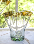 A clear glass vase with gold ribbon rim, placed on a table with a bright background, showcasing its unique shape and reflective gold detailing.