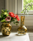 Kitchen sink with brass faucet, flowers in vases covered in 14k gold leaf, and window in the background