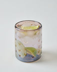 Glass with a drink, lime wedge, and ice cubes on a light gray background