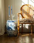 Decorative blue and white jar with candles on a small table next to a wicker chair with a patterned cushion.