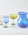 Set of colorful glassware including a pitcher and various glasses on a light background
