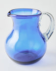 Blue glass pitcher with clear handle on a white background