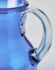 Close-up of a blue glass pitcher with a clear handle on a light gray background