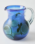 Blue glass pitcher with clear handle with lime slices and mint leaves on a white background