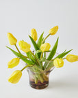 Pink glass vase with yellow tulips on a light gray background