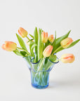 Bouquet of peach-colored tulips in a blue glass vase on a light background