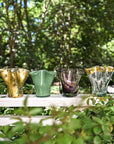 Vases in different styles lined up in front of greenery