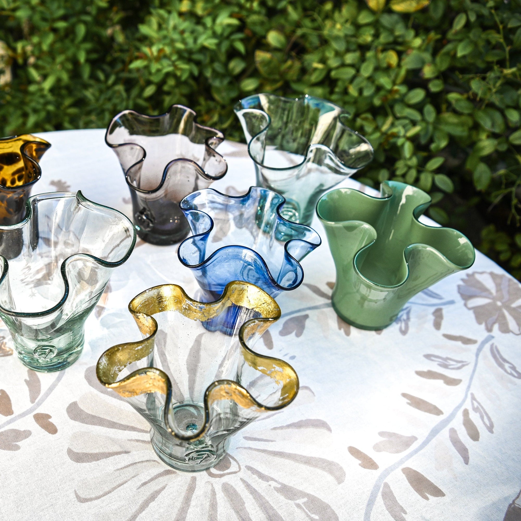 Colorful glass vases on a table outdoors with greenery in the background