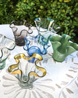 Colorful glass vases on a table outdoors with greenery in the background