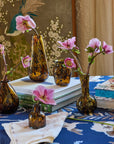 A collection of brown tortoise patterned glass vases of various sizes arranged on a table with a blue floral tablecloth, displaying pink flowers.