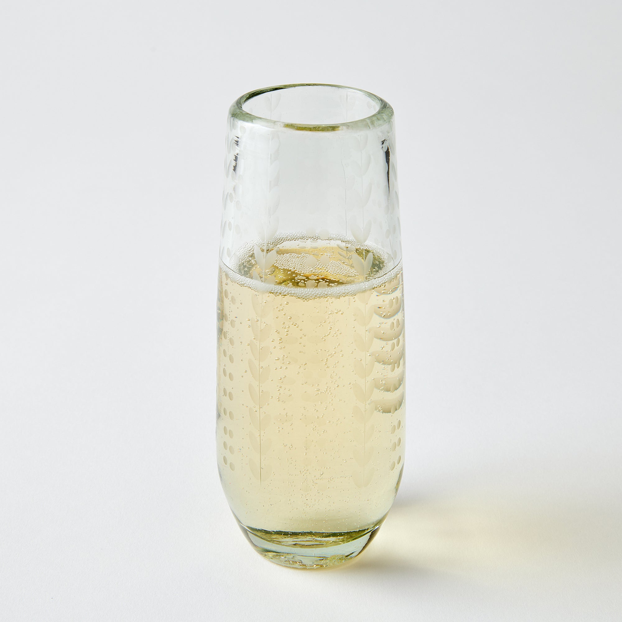 Clear glass etched with ferns and dots filled with champagne on a light gray background
