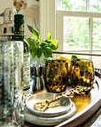 Alcohol bottles, glasses, and bar tools on a wooden surface with a window in the background