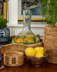 Decorative items including glass decanter, wicker baskets, lemons, and a vase on a table with a blurred indoor background.
